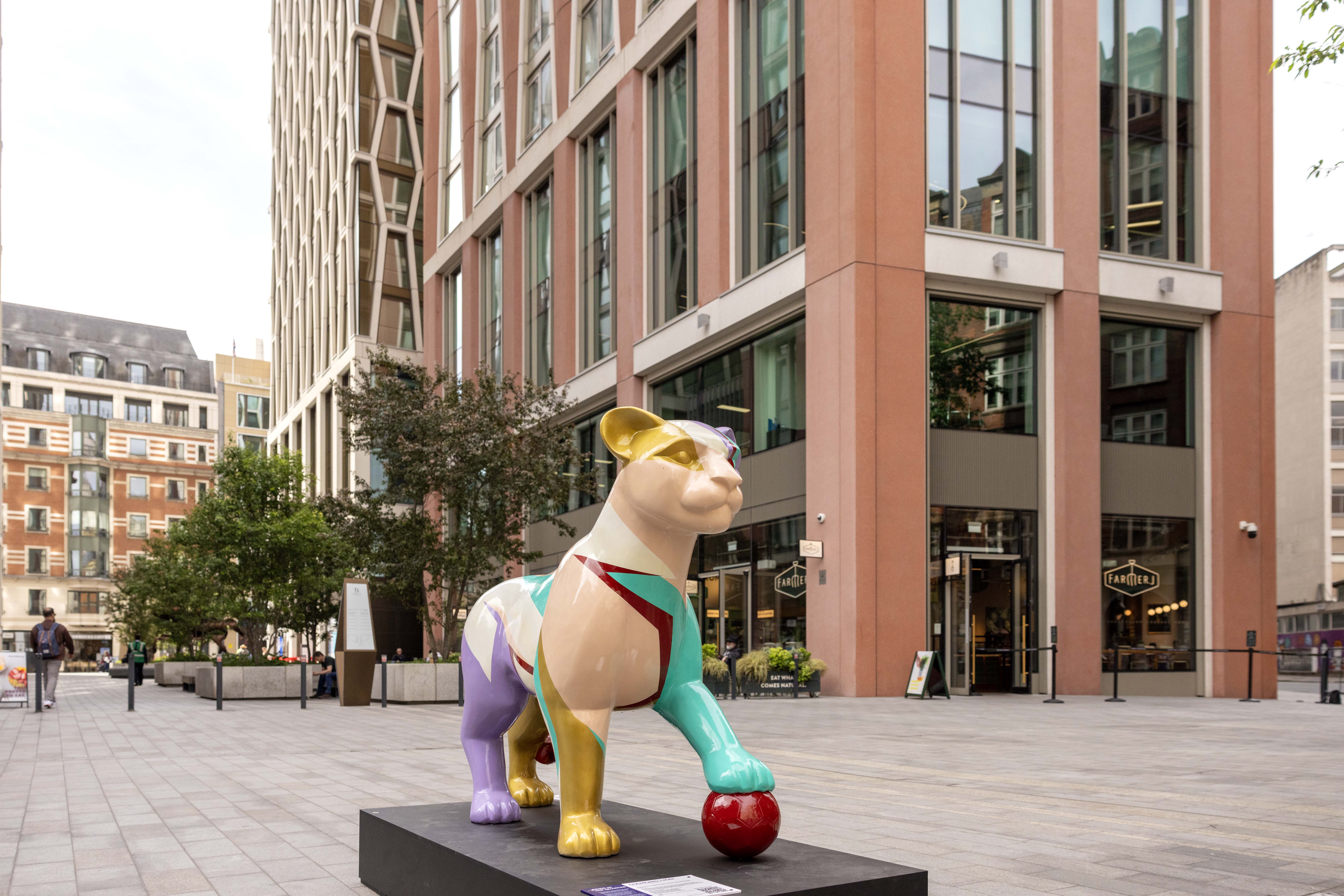 Colourful Lion sculpture on display in an urban plaza (The Broadway, St James's), set against a backdrop of modern buildings, evokes a lively and artistic atmosphere.