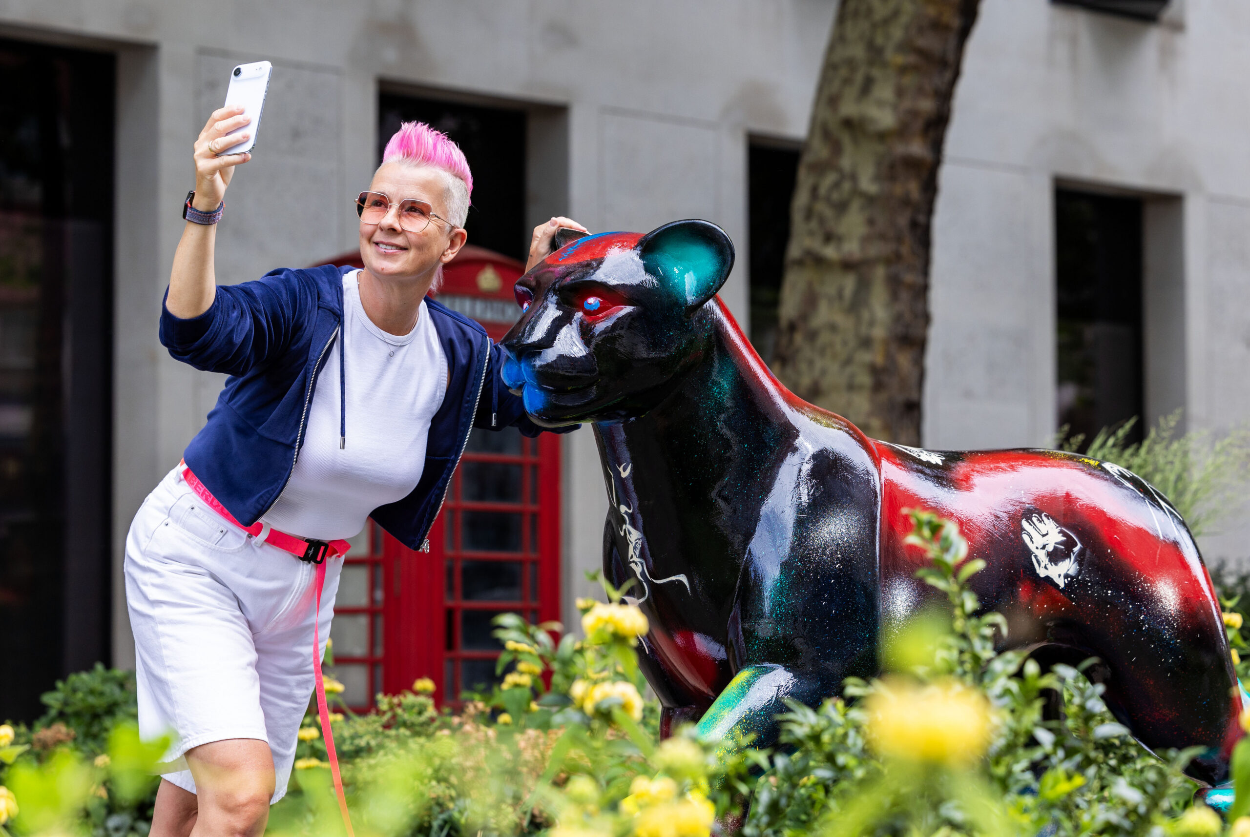 Lady poses with lion sculpture on Strand Aldwcyh to take a selfie. Lion is mainly coloured black with red accents.