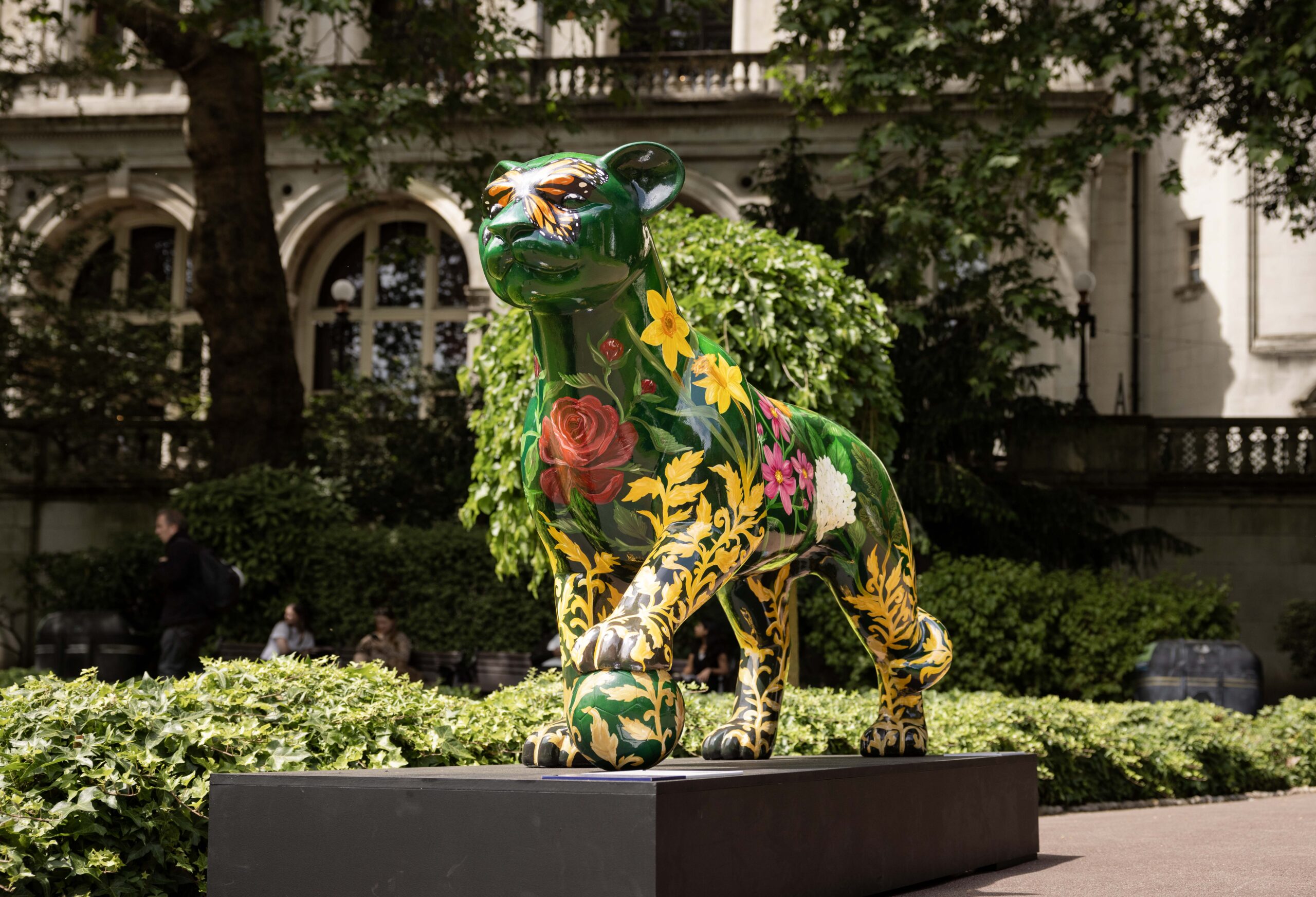 Lioness sculpture decorated with green paint with yellow detailed flowers and red roses stands tall in Whitehall Gardens